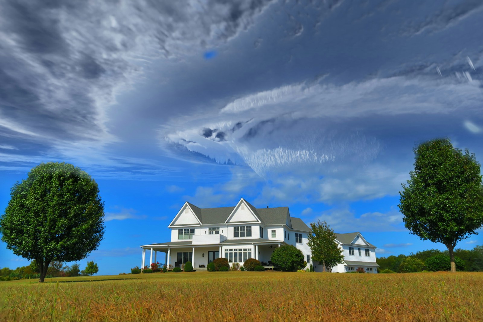 white and gray house between two green tall trees under gray clouds forming swirl during daytime homeowners
