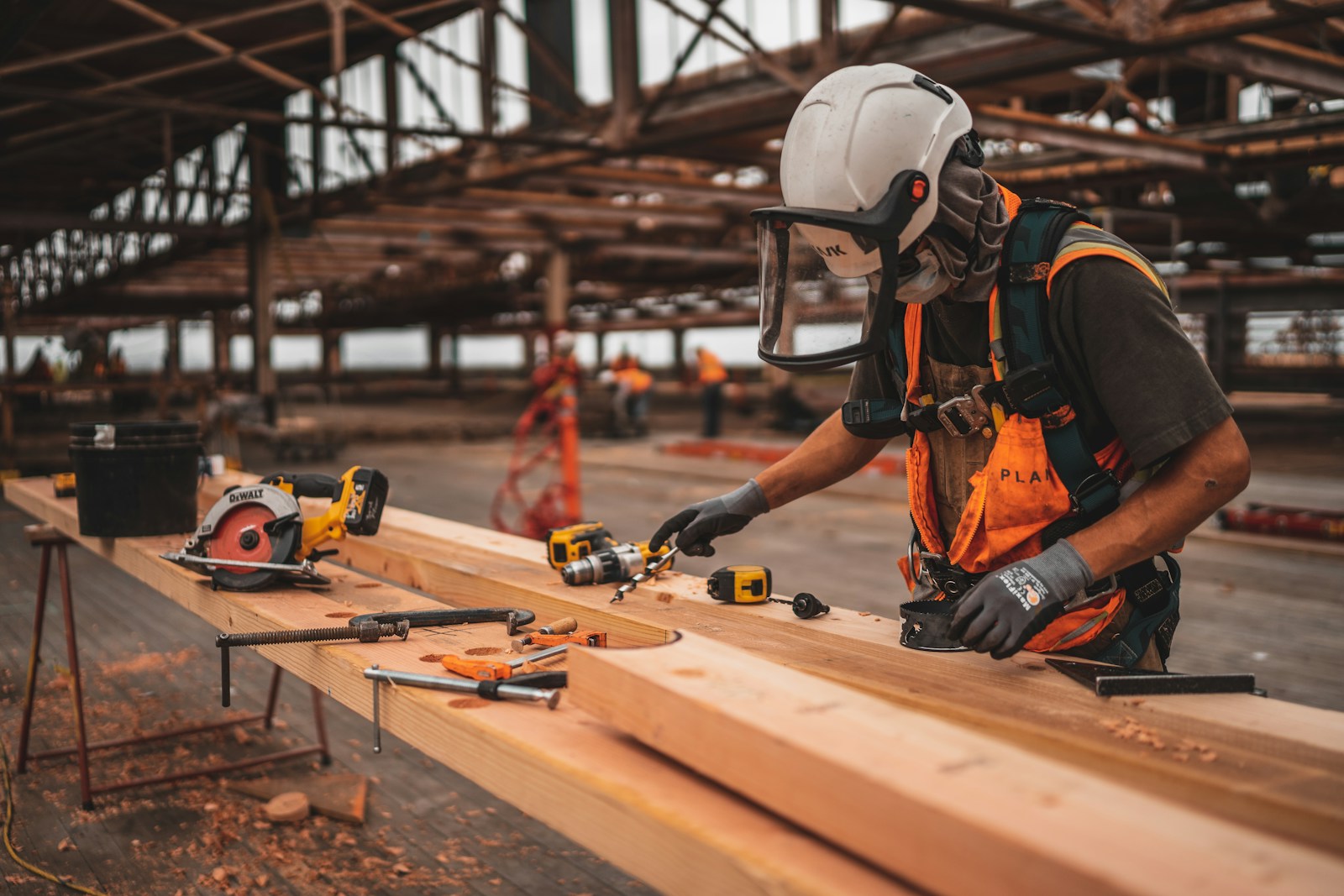 man in orange and black vest wearing white helmet holding yellow and black power tool, artisan contractors
